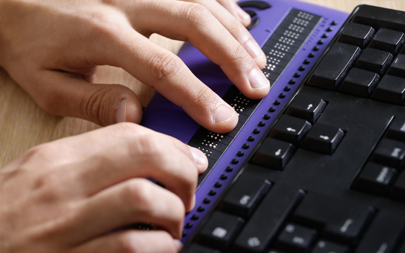 Blind person using computer with braille computer display and a computer keyboard.